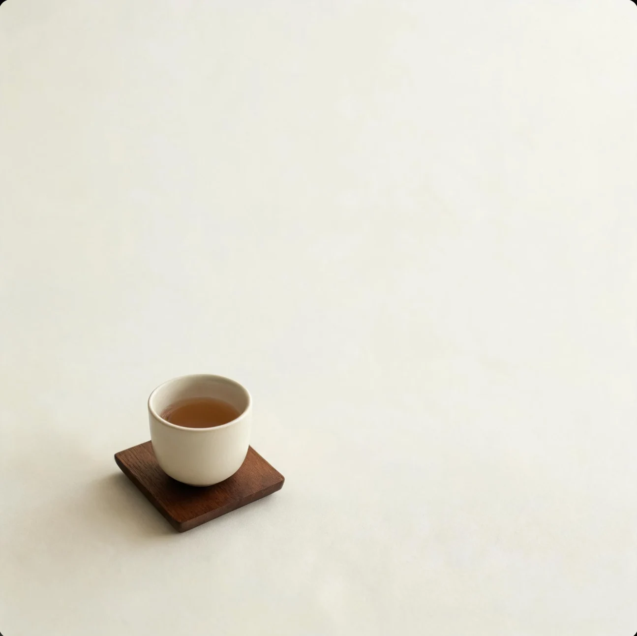 一只盛着棕色液体的白杯放在木杯垫上,周围是大面积浅色桌面。